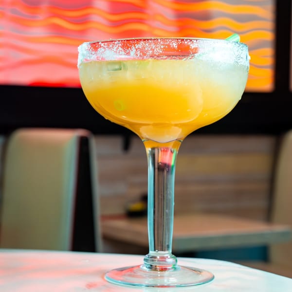 Close-up of a vibrant yellow margarita with a salted rim and green straw, on a table at Mama's Tacos Delicioso.