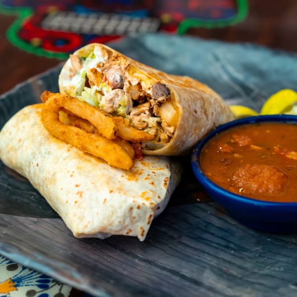 Two Mama's Tacos Delicioso burritos with fries and a side of salsa on a dark plate.