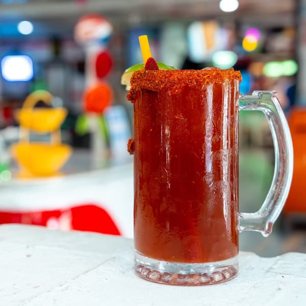 A large glass mug of Mama's Tacos Delicioso michelada, garnished with chili powder and lime.