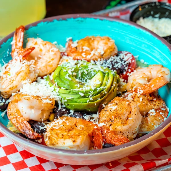 Shrimp and avocado salad with black beans and cheese in a turquoise bowl on a red checkered napkin.