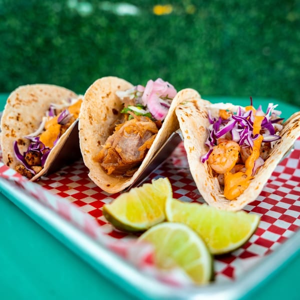 Three Mama's Tacos with various fillings, cabbage, and sauce, served with lime wedges.